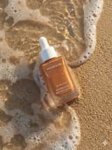 Photographie ultra-réaliste de produits de soin sur du sable de plage humide